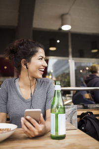 Happy woman wearing headphones resting at sidewalk cafe