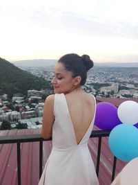 Young woman standing by cityscape against sky