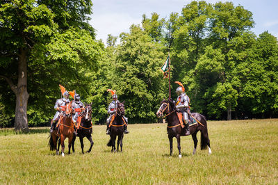 Men riding horses on field against trees