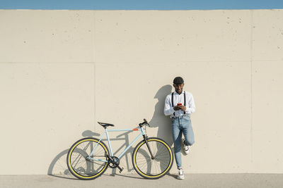 Man with bicycle using smart phone in front of wall