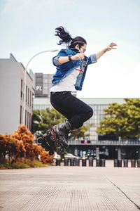 Young woman jumping in mid-air against sky in city