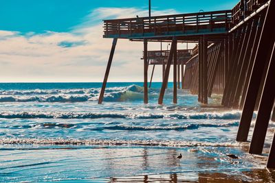Pier over beach against cloudy sky