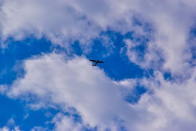 Low angle view of airplane flying in cloudy sky