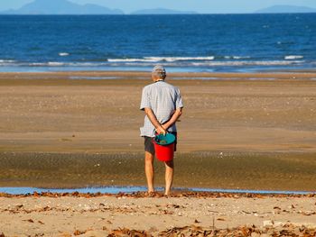 Rear view of man with bucket standing at beach