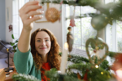 Smiling woman decorating christmas tree at home