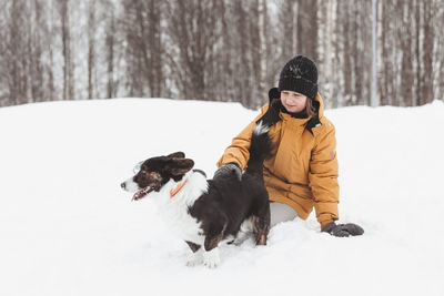 A girl plays with a corgi dog in a winter park