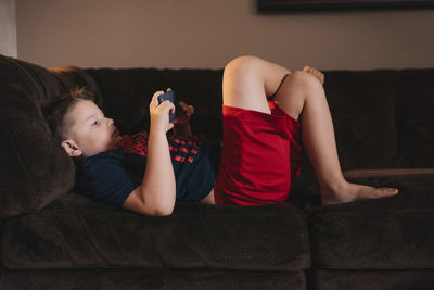 Boy using mobile phone while lying on sofa at home