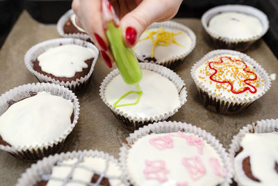 A woman squeezes colored frosting from a tube onto chocolate brown cupcakes covered white frosting.