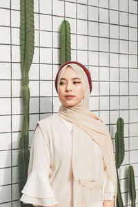 Young woman in hijab looking away against wall