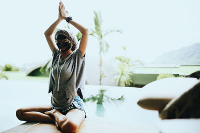 Portrait of woman wearing facial mask while doing yoga against sky