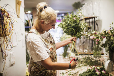 Female florist cutting plant stem while working in flower shop