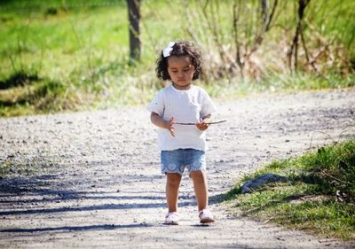 Full length of girl holding stick while walking on road