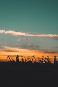 Silhouette cranes against sky during sunset