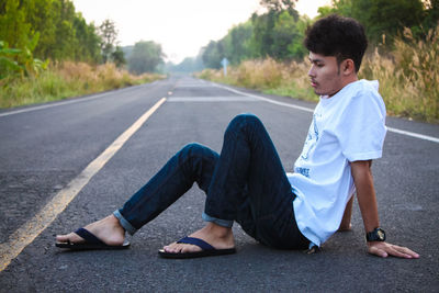 Side view of young man sitting on road