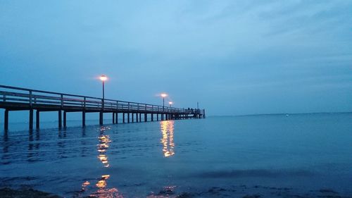 Illuminated pier over sea against sky at dusk