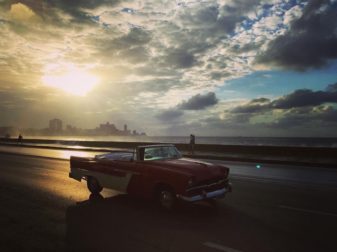 CAR ON ROAD BY SEA AGAINST SKY DURING SUNSET