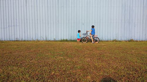 Brothers with bicycle on grassy field against wall