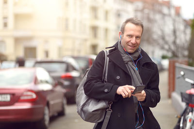 Portrait of smiling man listening music through headphones in city