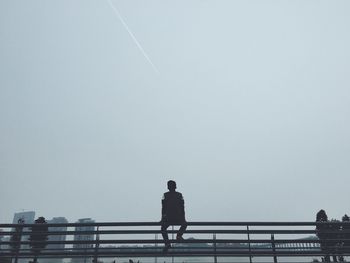 Rear view of man sitting on railing against sky