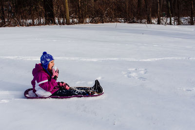 Side view of girl eating snow while sitting outdoors in winter