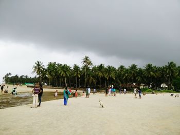 People walking on landscape against cloudy sky