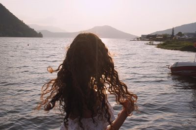 Rear view of woman standing at lakeshore against sky