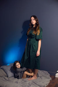 Mother and daughter in dresses sitting on a bed in a bedroom with a blue wall