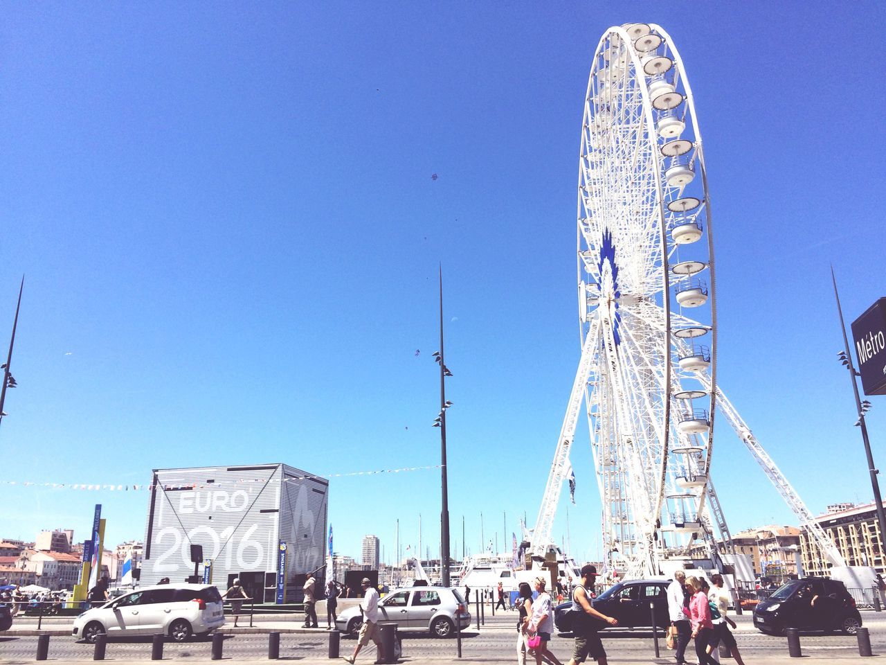 ferris wheel, amusement park, clear sky, amusement park ride, leisure activity, arts culture and entertainment, blue, copy space, built structure, architecture, large group of people, tourism, lifestyles, travel destinations, men, fun, enjoyment, travel, building exterior