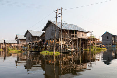 Stilt houses by buildings against clear sky