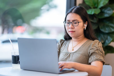 Portrait of young woman using phone while sitting on table