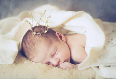 Close-up of cute baby girl sleeping with crown on bed