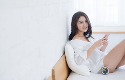 Portrait of young woman using phone while sitting on bed