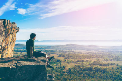Side view of man sitting on cliff against landscape