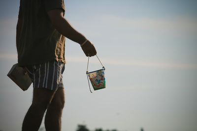 Midsection of man holding container against sky