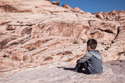 Rear view of boy sitting on rock