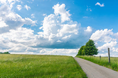 Empty road amidst field against sky