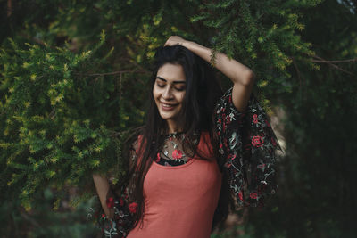 Smiling young woman standing against trees