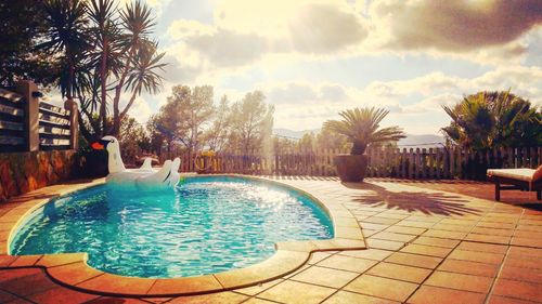 Swimming pool by palm trees against sky