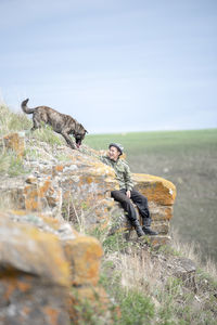 Man looking at dog while sitting on cliff at mountain