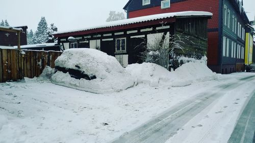 Snow covered houses by buildings in city