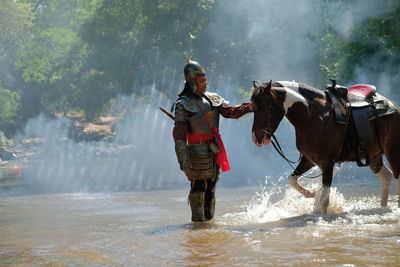 Man wearing armor standing with horse in river
