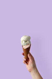 Cropped hand of woman holding ice cream cone against purple background