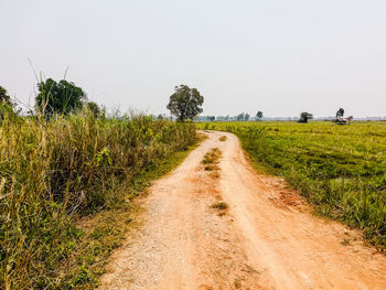 Dirt road amidst field against clear sky