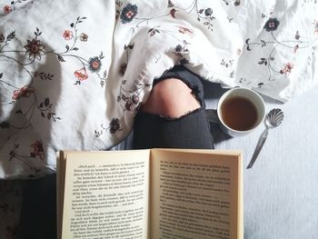 Midsection of woman with open book and coffee cup at home