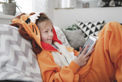 Smiling girl with digital tablet lying on sofa at home