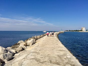 Rear view of woman walking on beach against blue sky