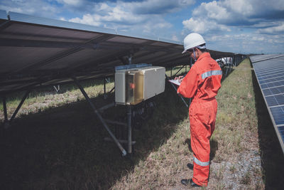 Side view of worker wearing reflective clothing while standing on solar panel against sky