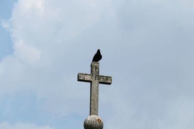 Low angle view of bird perching on cross against sky