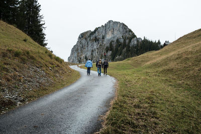 Rear view of people walking on road against clear sky