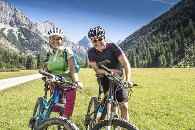 Portrait of smiling people with bicycle standing on field against mountains